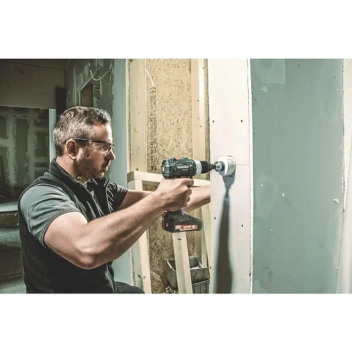 Metabo CAS 18V Akku-Bohrschrauber BS 18 LT BL - 18 V, Ohne Akku - Ein Mann bohrt mit einer Metabo-Bohrmaschine ein Loch in eine Wand. Die Bohrmaschine ist mit einem Aufsatz für das Bohren großer Löcher versehen.