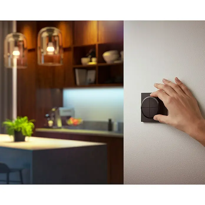 Philips Hue Lichtsteuerung Tap Dialswitch - 6 x 6 x 2 cm, Smart Home-fähig: Ja, Schwarz, Dimmbar - Eine Hand bedient einen stilvollen, dunklen Wandschalter mit Drehknopf in einem modernen Küchenambiente.