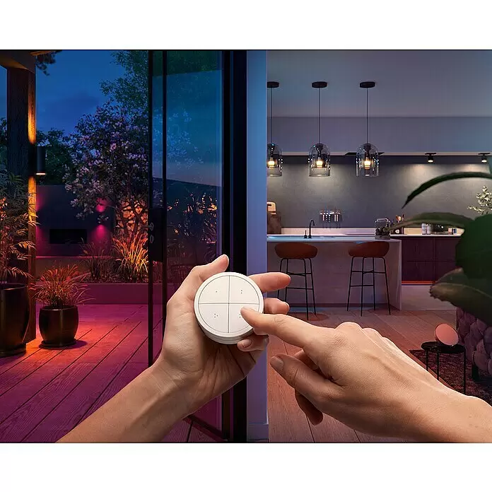 Philips Hue Lichtsteuerung Tap Dialswitch - 6 x 6 x 2 cm, Smart Home-fähig: Ja, Weiß, Dimmbar - Eine Hand hält eine weiße, runde Smart-Home-Fernbedienung mit vier Tasten und drückt eine davon, um farbige Innen- und Außenbeleuchtung zu steuern.