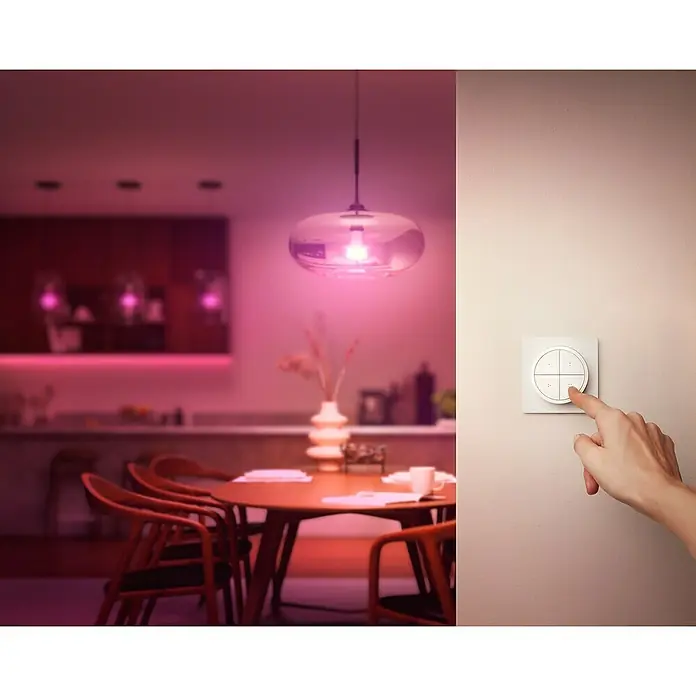 Philips Hue Lichtsteuerung Tap Dialswitch - 6 x 6 x 2 cm, Smart Home-fähig: Ja, Weiß, Dimmbar - Eine Person bedient eine Hue Smart Switch an der Wand, während eine Lampe im Hintergrund in leuchtendem Pink erstrahlt.