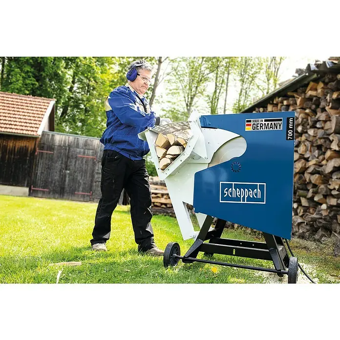 Scheppach Wippkreissäge HS720 - 4.500 W, Durchmesser Sägeblatt: 700 mm - Ein Mann bedient eine Scheppach Wippsäge mit Holz. Die Maschine ist blau und weiß, im Hintergrund Holzstapel und Grün.