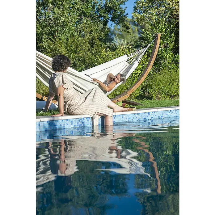 La Siesta Hängematte Modesta - L x B: 350 x 160 cm, Latte, Double - Zwei Frauen entspannen am Pool, wobei eine in einer Hängematte liegt. Die Hängematte ist der Mittelpunkt und lädt zum Verweilen ein.