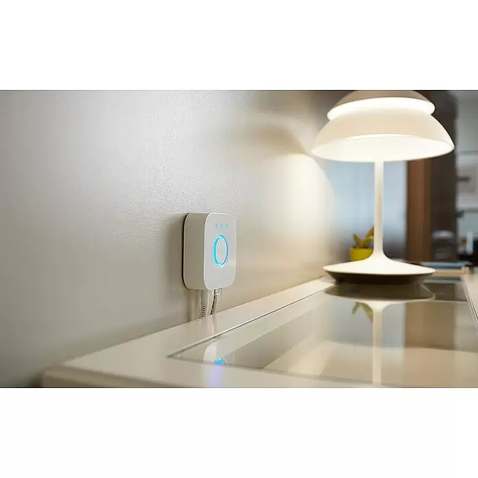 Philips Hue Smart-LED-Lampen-Set White & Color Ambiance - E27, Dimmbar, Warmweiß, 806 lm - 1.055 lm, 9 W - Weißer Philips Hue Bridge mit leuchtenden blauen Lichtern, über Ethernet-Kabel an einer Wand verbunden.