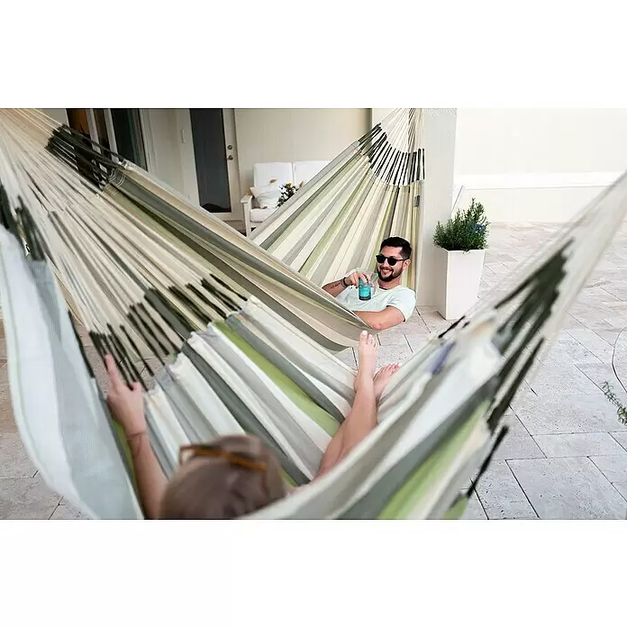 La Siesta Hängesessel Domingo Comfort - Zeder - Zwei Personen entspannen in gestreiften grünen und cremefarbenen Hängematten auf einer Terrasse.
