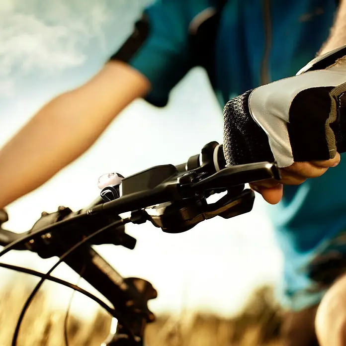 T'nB Linterna para bicicletas - Blanco - Primer plano de un manillar de bicicleta con un timbre y una mano con un guante de ciclismo, centrándose en los accesorios de la bicicleta para la seguridad.
