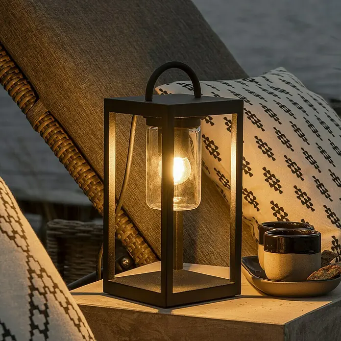 Konstsmide Metall-Laterne Bologna - 14 x 14 x 33 cm, Schwarz - Elegante schwarze Laterne mit Glühbirne auf einem Tisch, perfekt für gemütliche Abende im Freien. Dekorative Beleuchtung für Garten und Terrasse.