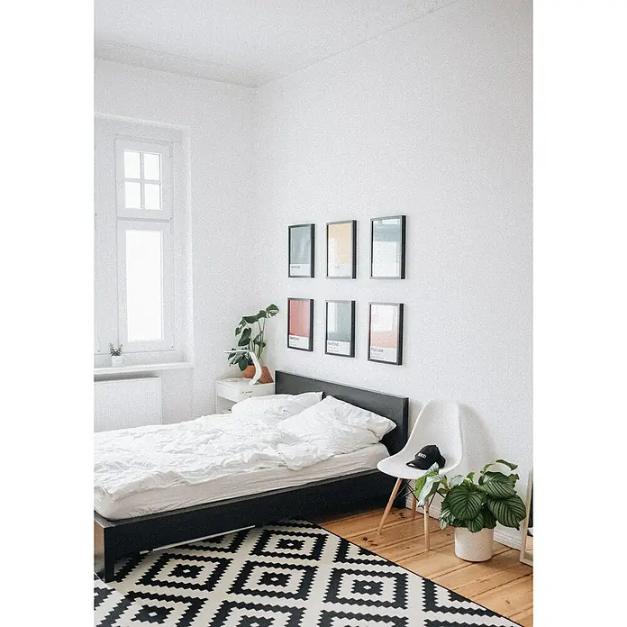 Titanlux Pintura para paredes Blanco Luminoso - Blanco luminoso, Mate, 15 l - Dormitorio con cama negra, una alfombra geométrica y seis muestras de color enmarcadas en la pared blanca.