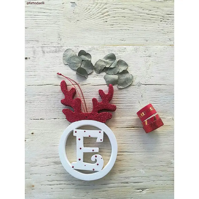 Fleur Purpurina Glitter - Cherry Red, 90 g, Brillante - Adorno navideño festivo con una "E" blanca y astas rojas, complementado con hojas de eucalipto y cinta roja sobre madera clara.