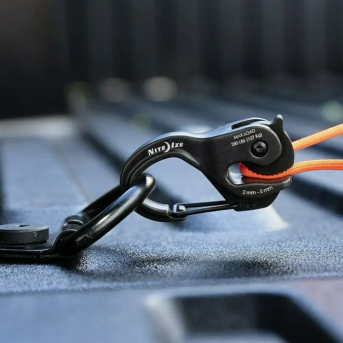 Nite Ize Karabinerhaken CamJam XT - Aluminium - Nahaufnahme eines Nite Ize Figure 9 Karabiners mit einem orangefarbenen Seil, der an einer Oberfläche befestigt ist.