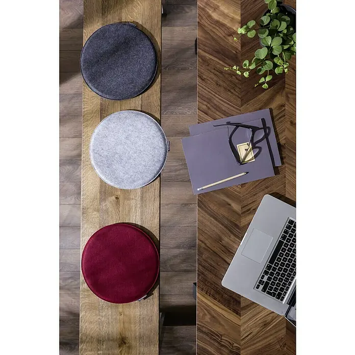 Sitzkissen rund Carl - Ø x H: 35 x 2 cm, Grau, 100 % Polyester - Drei runde Sitzkissen in Anthrazit, Grau und Rot auf einem Holztisch, daneben ein Laptop und Notizen.