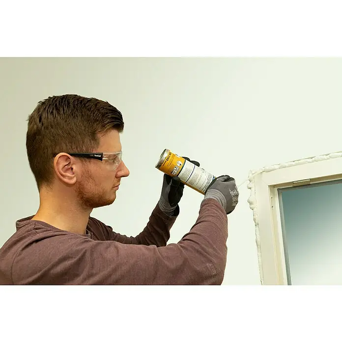Sika Bauschaum 1-K PU - 300 ml - Ein Mann dichtet mit Bauchaum ein Fenster ab, um es zu isolieren. Er trägt dabei eine Schutzbrille und Handschuhe.