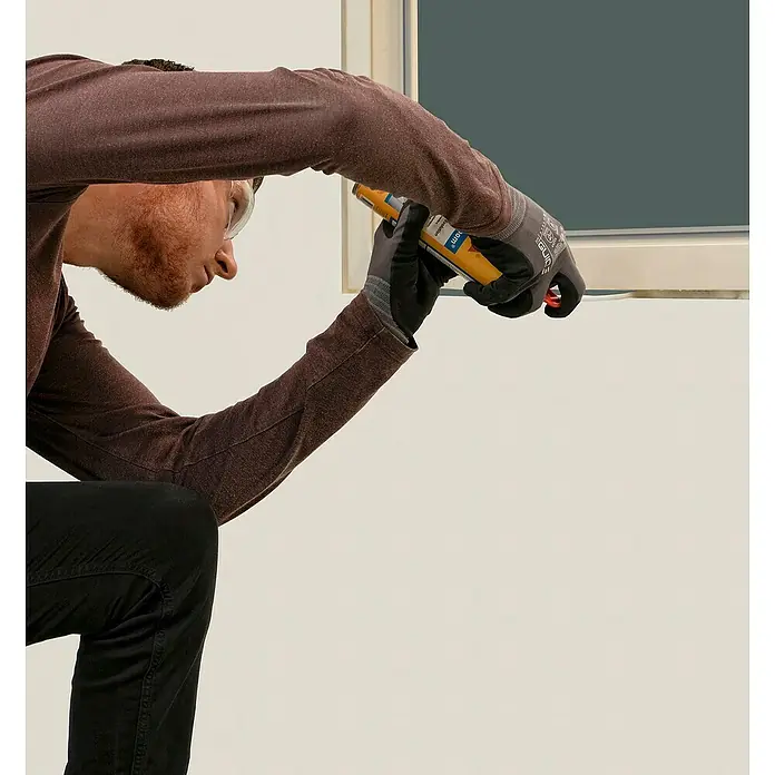 Sika Bauschaum 1-K PU - 300 ml - Handwerker dichtet mit einer gelben Kartusche eine Fensterfuge ab, Schutzbrille und Arbeitshandschuhe schützen ihn.
