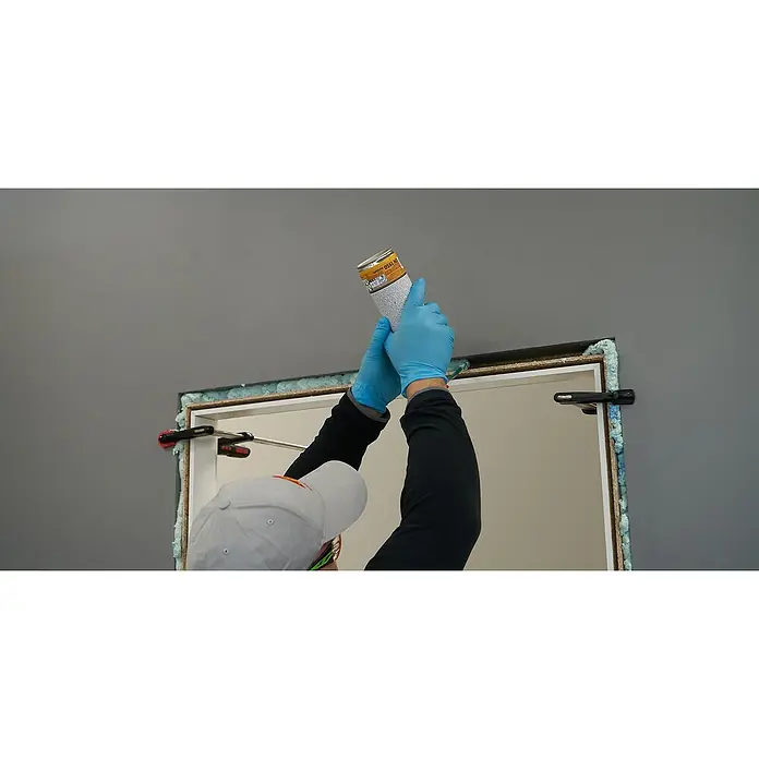 Sika 2K-Montageschaum BOOM-156 2C - 400 ml - Eine Dose Bauschaum wird von einem Handwerker mit blauen Handschuhen über einen Türrahmen gesprüht, der mit Schaumstoff abgedichtet ist.