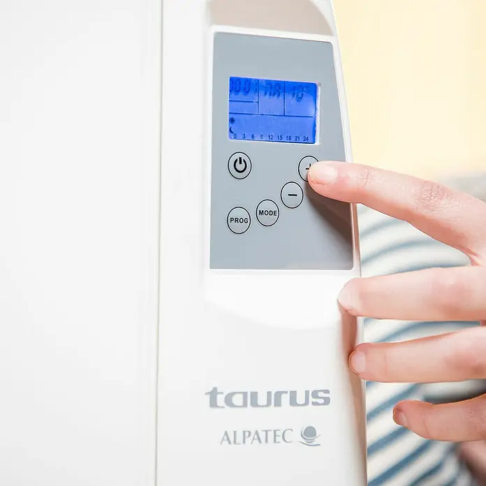Taurus Konvektorheizung Malbork - 1.200 W, Raumgröße bis ca. 12 m², Weiß - Nahaufnahme einer Taurus Alpatec Heizung mit digitaler Steuerung, die von einer Hand bedient wird.