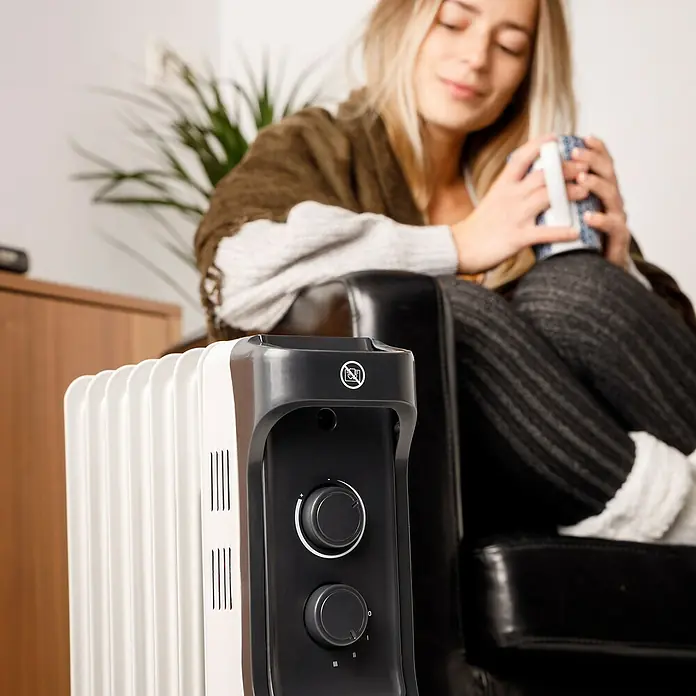 Taurus Ölradiator New Dakar - 2.000 W, Raumgröße bis ca. 20 m², Weiß - Nahaufnahme einer Heizung im Raum, während eine Frau entspannt im Hintergrund sitzt.