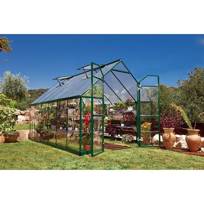 Palram – Canopia Gewächshaus Balance - Außenmaß inkl. Dachüberstand (B x T): 244 x 367 cm, 0,7 mm, Grün - Ein großes Gewächshaus aus Glas und grünem Metall steht im Garten, voller Pflanzen und Blumen, bereit für den begeisterten Gärtner.