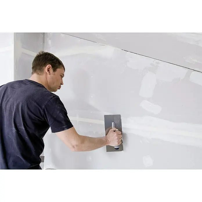 Knauf Feinspachtel Uniflott Finish - 20 kg, Gebrauchsfertig - Ein Handwerker glättet sorgfältig Spachtelmasse an einer Wand mit einem professionellen Glättspachtel, um eine ebene Oberfläche zu schaffen.