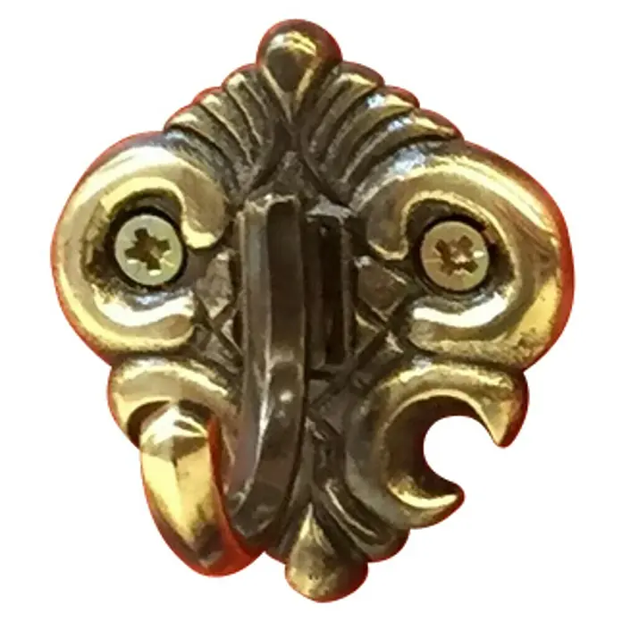 Häfele Gancho para colgar - Altura: 55 mm, Latón - Primer plano de un gancho de pared dorado y ornamentado con tornillos visibles, que combina funcionalidad con diseño decorativo.