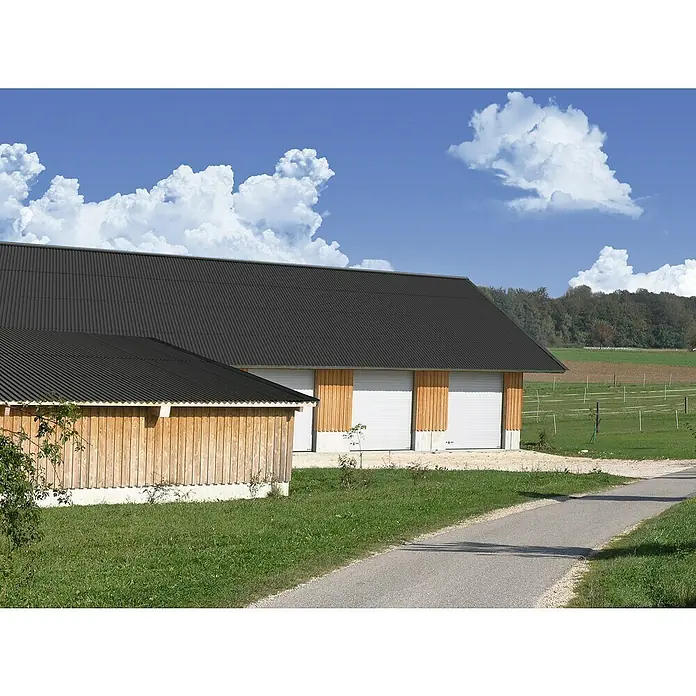 Gutta Wellplatte Shelltec - 200 cm x 95 cm x 4 mm, Anthrazit - Eine Ansicht eines Gebäudes mit einem schwarzen Metalldach und weißen Rolltoren mit Holzverkleidung an einer asphaltierten Straße.