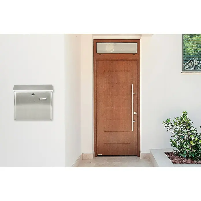 Burg-Wächter Wandbriefkasten Comfort 3913 - L x B x H: 38 x 14,8 x 34 cm, Edelstahl, Edelstahl, Öffnungsstopp - Ein moderner Briefkasten aus Edelstahl hängt neben einer braunen Haustür mit einem langen, silbernen Griff an einer weißen Wand.