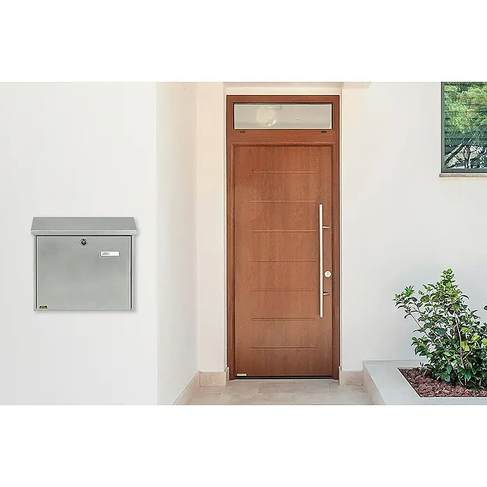 Burg-Wächter Wandbriefkasten Comfort 913 - L x B x H: 38 x 14,8 x 34 cm, Silber, Stahl, Öffnungsstopp - Silberner Wandbriefkasten mit Schloss und Namensschild an einer weißen Wand neben einer Haustür.