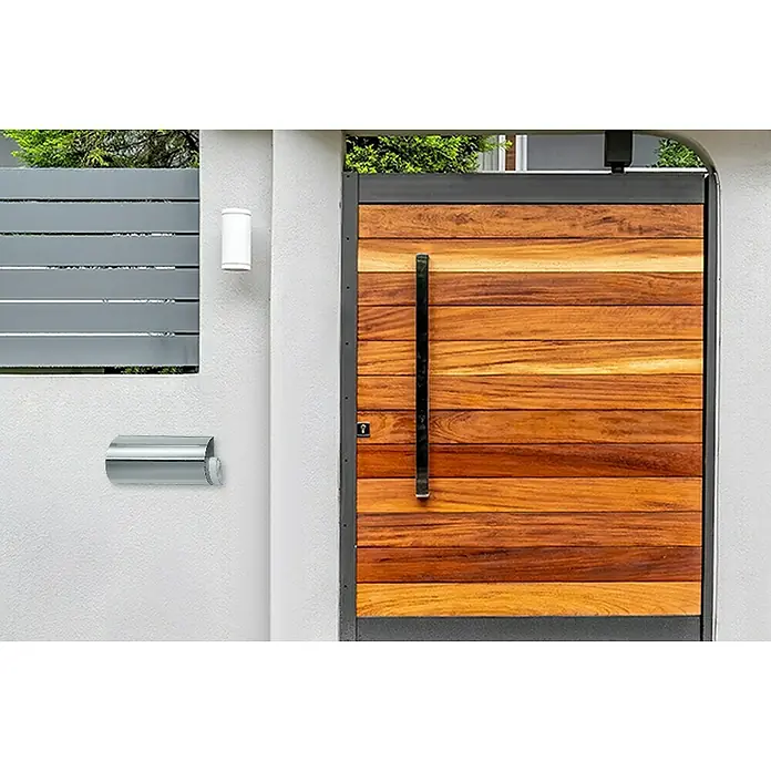 Portaferm Zeitungsbox - Edelstahl - Moderne Außentür mit Holzpaneelen, Metallrahmen und einem langen, schlanken Griff. Briefkasten und Wandleuchte sind ebenfalls sichtbar.