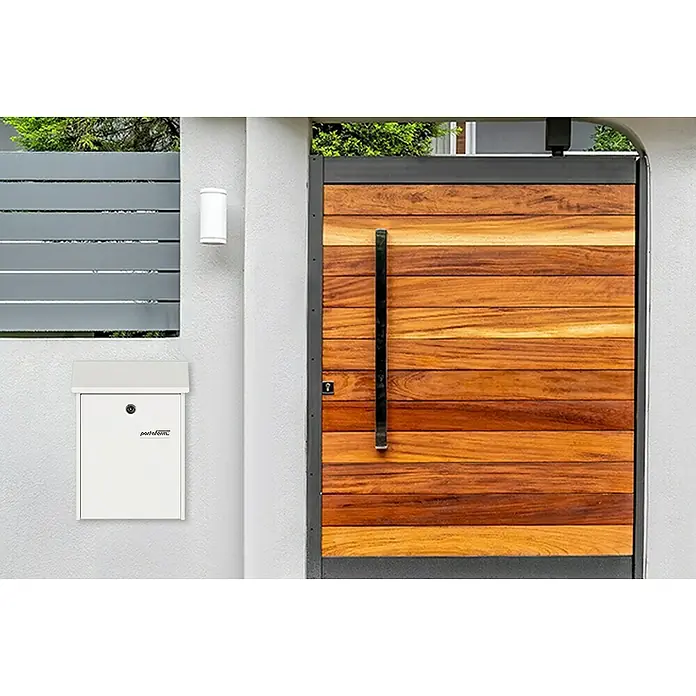 Portaferm Wandbriefkasten PF 22 - L x B x H: 7,5 x 22,5 x 30,5 cm, Weiß, Stahl - Das Bild zeigt eine moderne, weiße Briefkastenanlage an einer Wand neben einem Holztor. Der Briefkasten ist schlicht und funktional gestaltet.