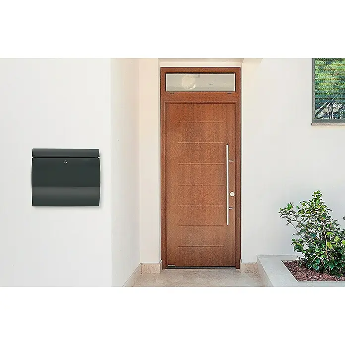 Burg-Wächter Wandbriefkasten Toscana 856 - L x B x H: 10,6 x 37,6 x 33 cm, Anthrazit, Stahl, Öffnungsstopp - Eine moderne Hausfassade mit einem anthrazitfarbenen Briefkasten links und einer Holztür mit einem langen Griff rechts.