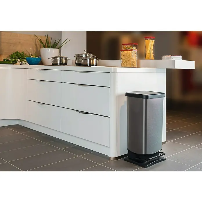 Cubo con pedal Paso carbono - 40 l, Plástico, Gris/Negro - Un moderno cubo de basura gris con pedal se encuentra en una elegante cocina con armarios blancos y baldosas grises.