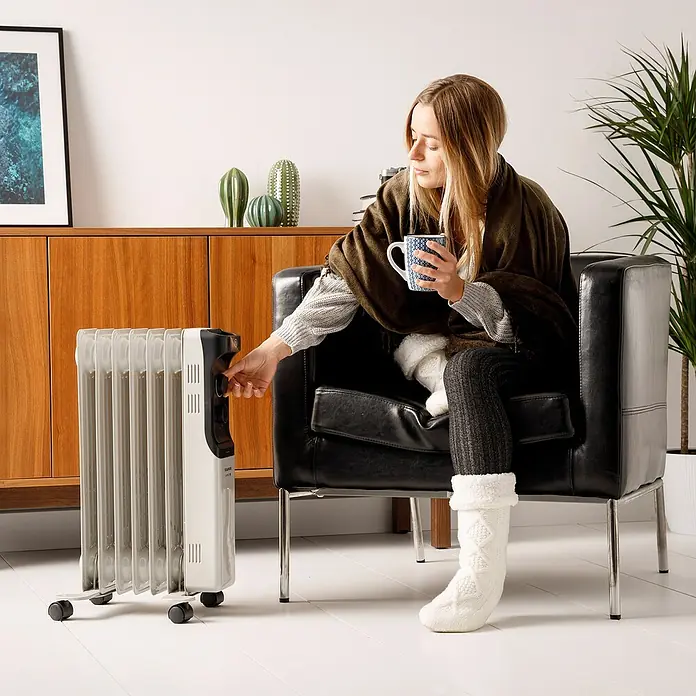 Taurus Ölradiator New Dakar - 2.000 W, Raumgröße bis ca. 20 m², Weiß - Frau reguliert einen weißen Ölradiator im Wohnzimmer, umgeben von Möbeln und einer Pflanze, für angenehme Wärme.