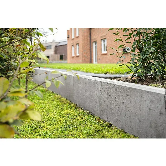 Diephaus L-Stein - 30 cm, 40 cm, Stärke: 7 cm, Grau - Bild einer grauen Garteneinfassung aus Beton, die einen Rasen von einem Blumenbeet trennt, im Hintergrund ein Backsteinhaus.