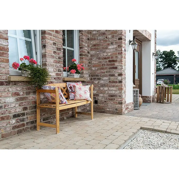Diephaus Pflasterstein Austin - Sandstein, 14 x 14 x 7 cm, Rechteckig - Eine charmante Holzbank mit Kissen vor einer rustikalen Backsteinmauer. Bietet einen einladenden Sitzplatz im Freien.