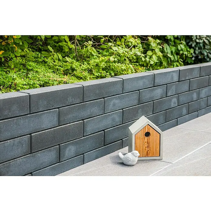 Diephaus Palisade / Mauerstein Laredo Meso - 80 x 10 x 10 cm, Basalt, Beton - Nahaufnahme einer modernen, grauen Gartenmauer mit einem dekorativen Vogelhaus und einer kleinen Vogelstatue. Die Mauer ist aus rechteckigen Steinen gefertigt.