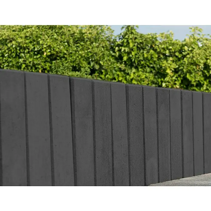 Diephaus Palisade / Mauerstein Laredo Meso - 80 x 10 x 10 cm, Basalt, Beton - Ein moderner grauer Betonsichtschutzzaun mit vertikalen Linien und grüner Hecke im Hintergrund. Ideal für stilvolle Privatsphäre.