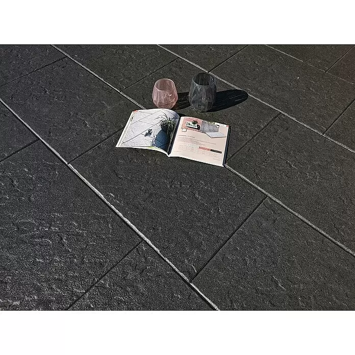Diephaus Terrassenplatte Glandale - 40 x 40 x 4 cm, Schwarz/Basalt, Beton - Strukturierte dunkelgraue Outdoor-Fliesen mit hellen Fugen, darauf ein Magazin und Gläser.