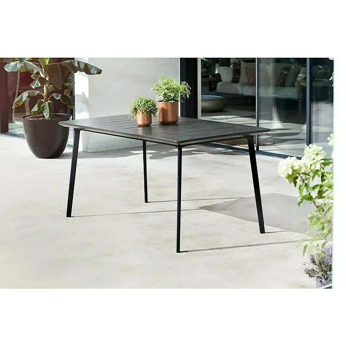 Keter Mesa de jardín Metalea - L x An x Al: 146,5 x 87 x 75 cm, Polipropileno, Marrón - Una mesa rectangular de exterior con tablero oscuro y patas negras, decorada con dos plantas en macetas de cobre.