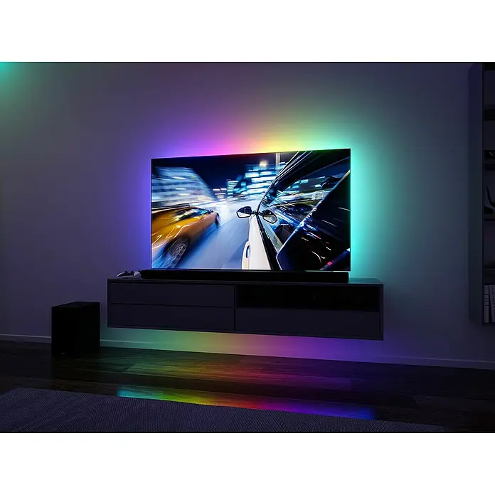 Paulmann LED-Band EntertainLED 55 Zoll - Länge: 200 cm, Lichtfarbe: RGB, 3,5 W - Ein moderner Fernseher mit Ambilight-Technologie zeigt ein schnelles Autorennen, das die Farben dynamisch an die Umgebung anpasst.