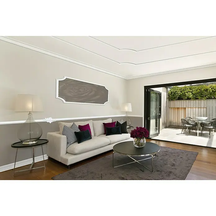 Zierprofil Modern E 36 - 2 m x 40 mm x 40 mm, XPS-Hartschaumplatten - Elegantes Wohnzimmer mit stilvoller Couch, Tisch und Dekorationen. Die Einrichtung strahlt Komfort und modernes Design aus.