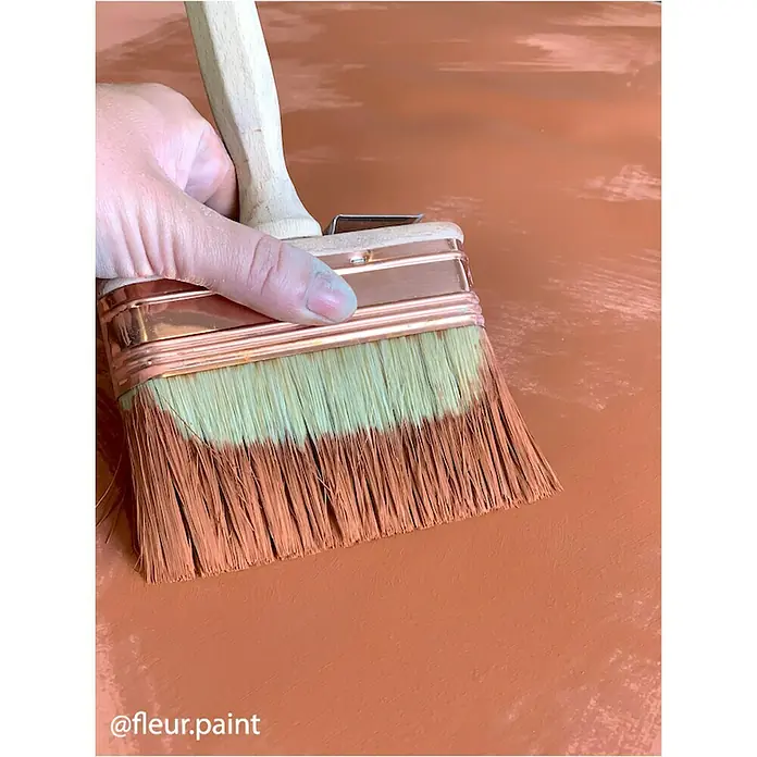 Fleur Pintura para efectos decorativos Lime Paint - Grand Canyon, 750 ml, Mate - Primer plano de un pincel ancho con mango de madera, parcialmente sumergido en pintura terracota, sobre un fondo terracota.