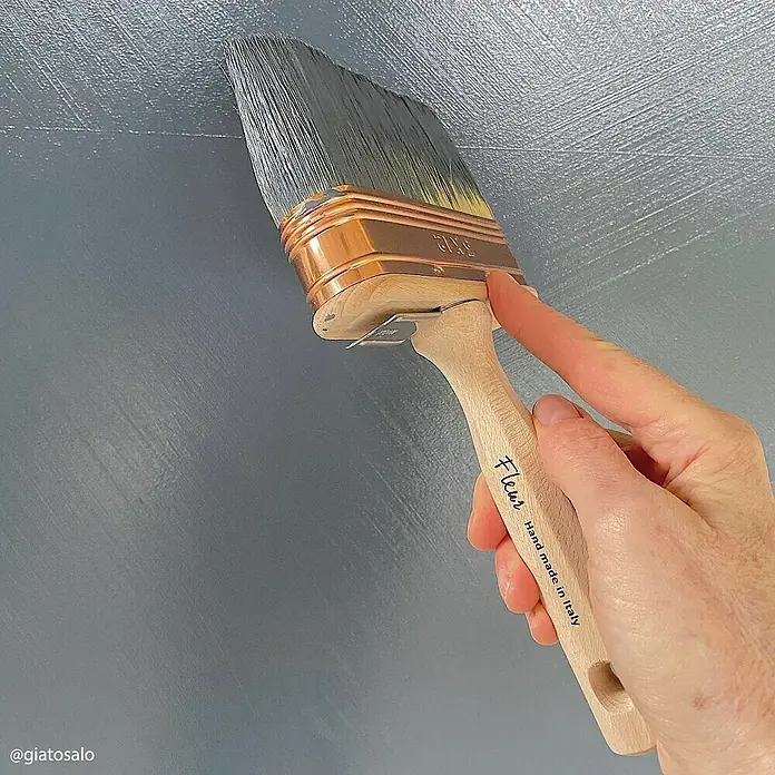 Fleur Pintura para efectos decorativos Lime Paint - Whale Song, 750 ml, Mate - Primer plano de un pincel Fleur que se utiliza para pintar sobre una superficie texturizada de color gris azulado. Hecho a mano en Italia.