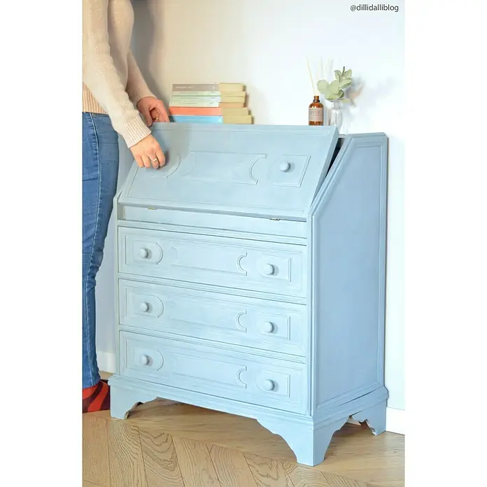 Fleur Pintura para efectos decorativos Lime Paint - French Mood, 750 ml, Mate - Un escritorio azul con superficie de escritura abatible y tres cajones de estilo shabby-chic. Libros y decoración encima del mueble.