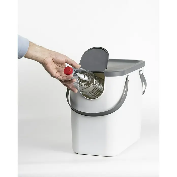 Rotho Albula Mülltrennsystem - 25 l, Kunststoff, Weiß - Ein Mann wirft eine Plastikflasche in einen weißen Recyclingeimer mit grauem Deckel und Griffen. Der Fokus liegt auf dem Mülleimer.