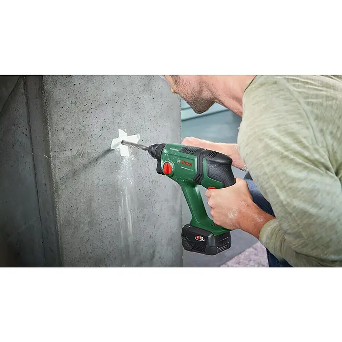 Bosch Power for All 18V Akku-Kombihammer UniversalHammer 18V - 18 V, Ohne Akku, 2 J - Ein Mann bohrt mit einem grünen Bosch Bohrhammer ein Loch in eine graue Betonwand. Der Akku-Bohrhammer ist gut sichtbar.