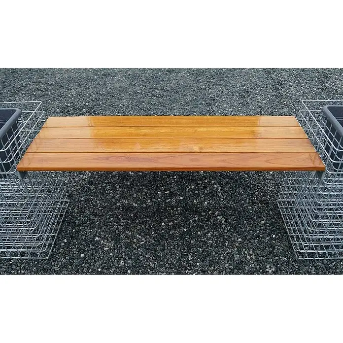 Gabiona Bankauflage - Länge: 115 cm, Goldbraun - Die Holzbank liegt auf einem Kiesuntergrund und wird durch zwei Metallkörbe getragen. Das Holz ist gelblich-braun und glänzend lackiert.