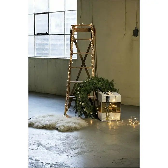 Konstsmide LED-Lichterkette - Innen, Lichtfarbe: Warmweiß, Anzahl Leuchtmittel: 35 Stk., Netzbetrieben, Transparent - Dekorativer Raum mit einer Holzleiter, Weihnachtskranz, Geschenk und Lichterkette, die eine festliche Atmosphäre schaffen.