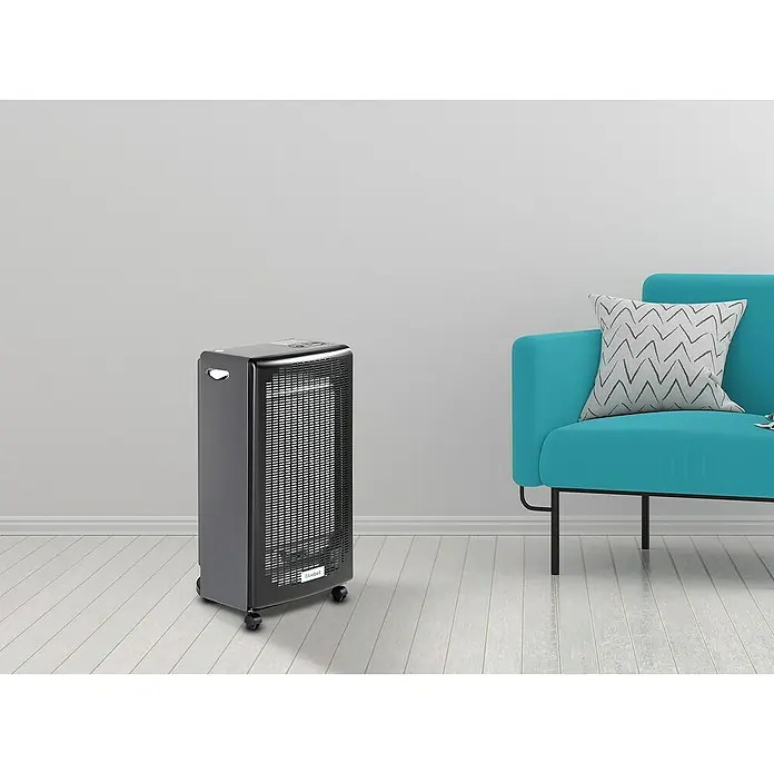 Estufa de gas llama azul Berna - 4,2 kW, Negro - Un elegante y portátil calefactor de espacio Bluebell en negro se encuentra junto a un sillón verde azulado, ofreciendo calidez y confort.