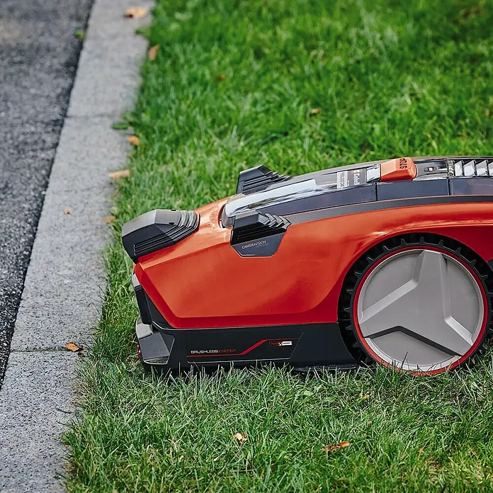 Einhell PXC 18V Mähroboter FREELEXO CAM 500 - 500 m², Schnittbreite: 18 cm, Kamera-gestützte Navigation - Ein orangeroter Mähroboter steht auf einem grünen Rasen neben einem Gehweg.