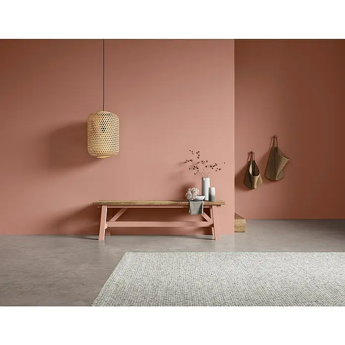 SCHÖNER WOHNEN-Farbe Naturell Wandfarbe Kreidefarbe - Herbstrascheln - gedecktes Rostrot, Matt, 2,5 l, Konservierungsmittelfrei - Eine moderne Inneneinrichtung mit einer stilvollen Bank, einer hängenden Lampe und dekorativen Elementen vor einer warmen, farbigen Wand.