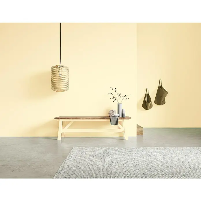 SCHÖNER WOHNEN-Farbe Naturell Wandfarbe KreidefarbeSommertag - strahlendes Hellgelb, Matt, 1 l, Konservierungsmittelfrei - Beige Wanddekoration mit einer stilvollen Bank, einer Hängelampe und dekorativen Accessoires.