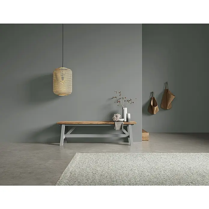 SCHÖNER WOHNEN-Farbe Naturell Wandfarbe Kreidefarbe - Donnerwetter - dunkles Grau, Matt, 2,5 l, Konservierungsmittelfrei - Einrichtungsidee mit einer Holzbank, einer hängenden Rattanlampe und Wanddekoration in einem Raum mit grauen Wänden und einem hellen Teppich.